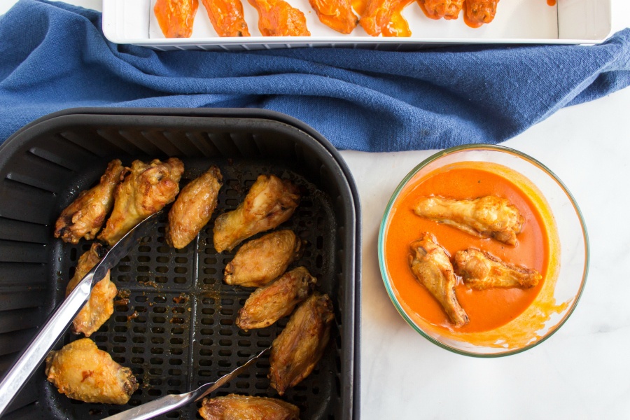 cooked chicken wings in air fryer and a side some wings being dipped in wing sauce