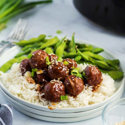 Crockpot Teriyaki Meatballs served over rice on a white plate, with a side of edamame