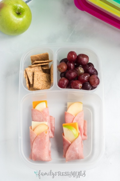 ham apple cheese wraps in a lunchbox with crackers and grapes