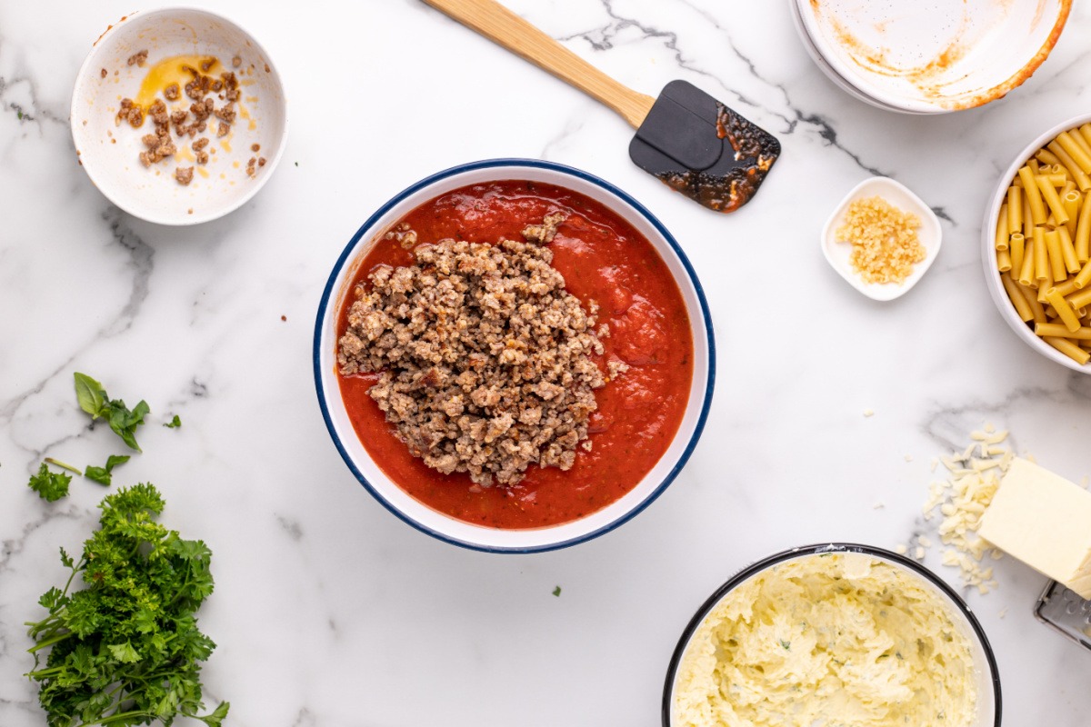 pasta sauce, diced tomatoes, cooked sausage, and water in a bowl