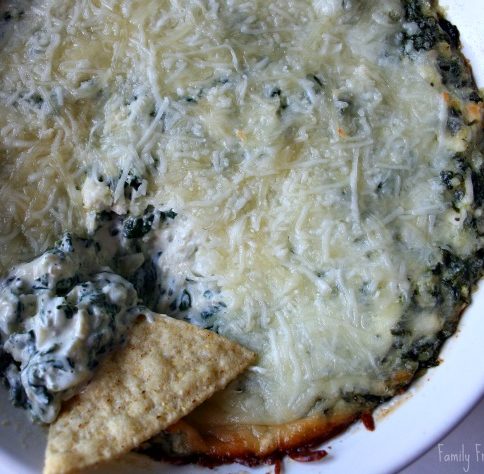 Spinach Artichoke Dip in a baking dish, with a tortilla chip scooping out some dip