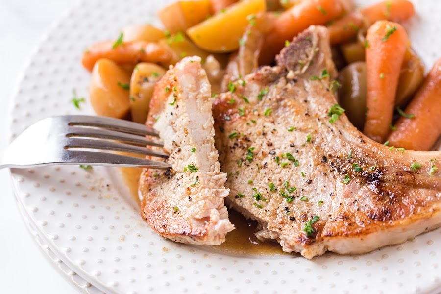 pork chop on a white plate with carrots and potatoes